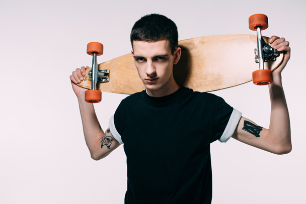 Hipster young guy holding longboard on shoulders isolated on white - Fotó, kép