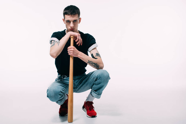 Young man sitting and leaning on baseball bat on white background - Fotó, kép