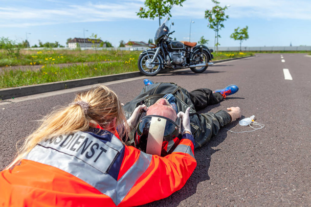 Немецкий парамедик снимает шлем с травмированного байкера. Мбаппе - немецкое слово для скорой помощи
. - Фото, изображение