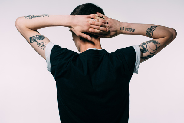 Hombre con tatuajes tomados de las manos detrás de la cabeza aislado en blanco
 - Foto, Imagen