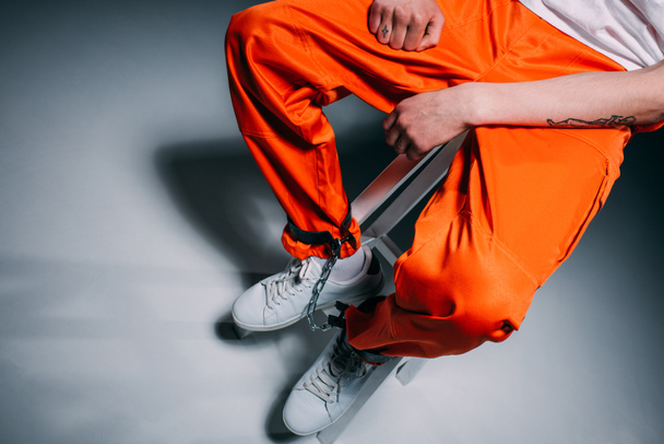 Draufsicht eines Mannes in orangefarbener Hose mit Manschetten an den Beinen, der auf einem Hocker auf dunklem Hintergrund sitzt - Foto, Bild