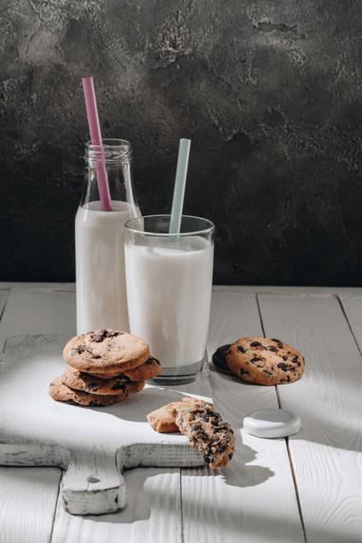 galletas con chispas de chocolate sobre tabla de cortar de madera blanca con leche
 - Foto, Imagen
