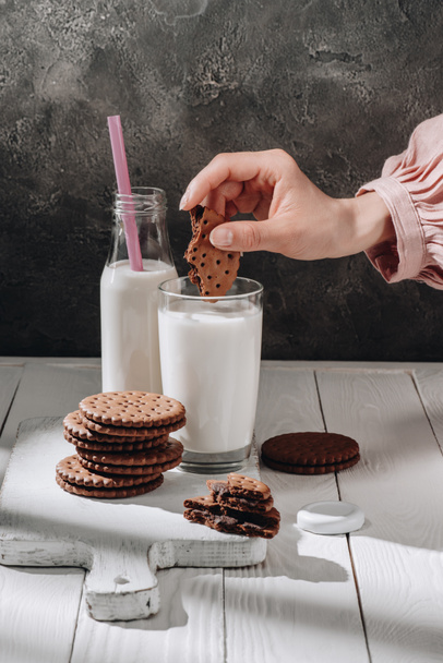 cropped shot of woman dipping delicious cookie into glass of milk - Фото, изображение