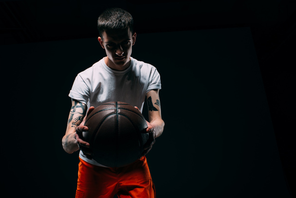 Man in prison uniform holding basketball ball on dark background - Fotografie, Obrázek
