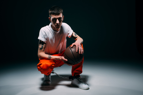 Man in orange pants and cuffs holding basketball ball on dark background - Photo, Image