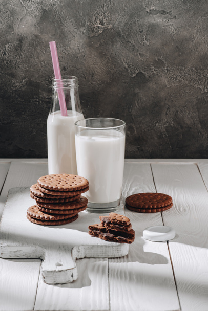 stack of delicious cookies with glass and bottle of milk on white wooden table - Foto, Bild