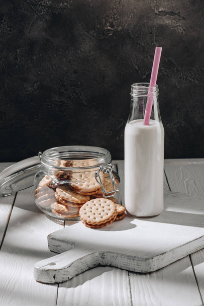 delicious cookies in glass jar with bottle of milk - Фото, изображение