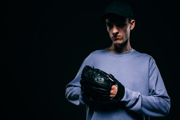 Handsome young man with baseball glove isolated on black - Фото, изображение