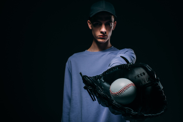 Le gars portant un gant de baseball montrant une balle de baseball isolée sur noir
 - Photo, image