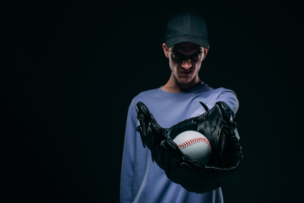 Hombre enojado usando guante de béisbol mostrando pelota de béisbol aislado en negro
 - Foto, Imagen
