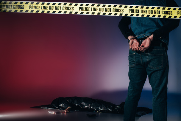 Rear view of murderer in cuffs behind police line on dark background - Photo, Image