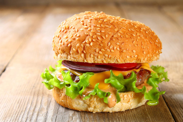 Hamburger maison savoureux composé de pain, galettes, salade, oignon rouge et tomate sur une vieille table en bois
. - Photo, image