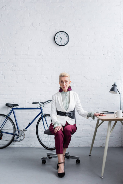 элегантная старшая деловая женщина, работающая в современном офисе с велосипедом
 - Фото, изображение