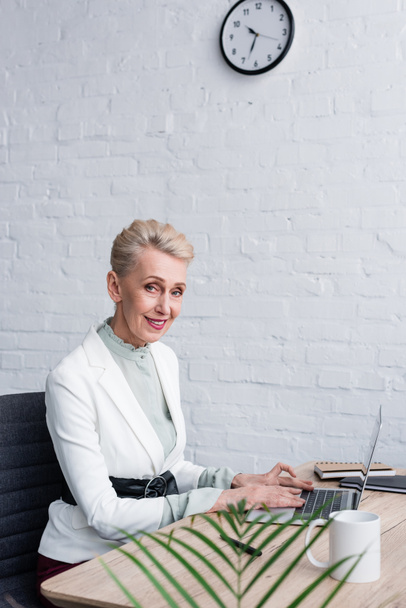 елегантна усміхнена бізнес-леді використовує ноутбук в сучасному офісі
 - Фото, зображення