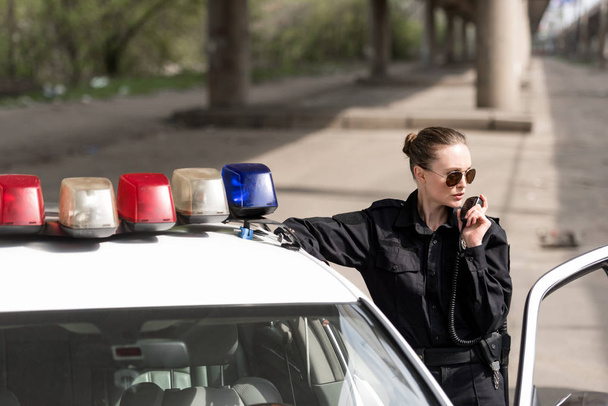 女性警察官がパトカーの近くのラジオで語っています。 - 写真・画像