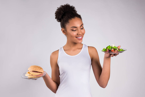 Černá dívka drží cheeseburger a salát, samostatný - Fotografie, Obrázek