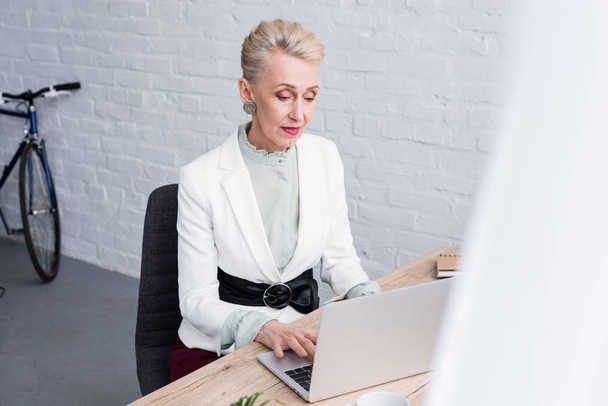 elegante senior zakenvrouw, werken met de laptop in kantoor - Foto, afbeelding
