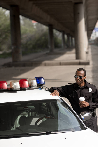 police officer with coffee to go leaning on police car on street - Foto, Imagen