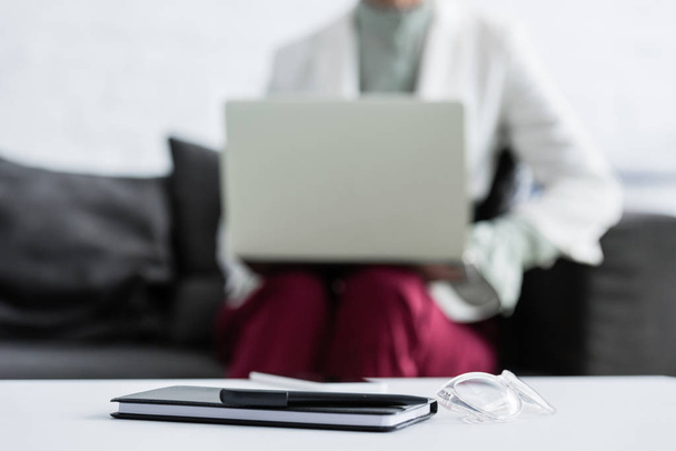 selektiver Fokus der Geschäftsfrau mit Laptop, Tagebuch, Stift und Brille auf dem Tisch im Vordergrund - Foto, Bild