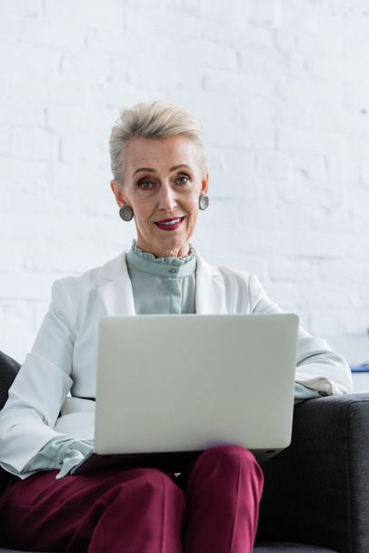 elegant senior businesswoman using laptop on sofa - Фото, изображение