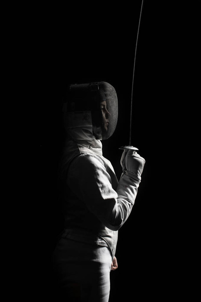 female fencer standing with sword on black background - Zdjęcie, obraz