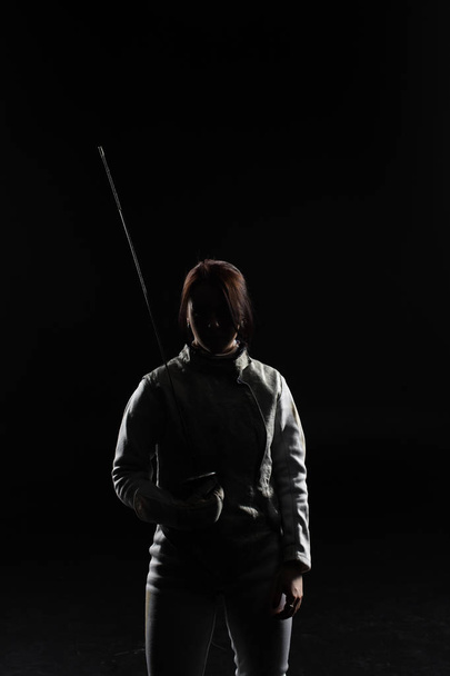 female fencer standing with sword on black background - Valokuva, kuva