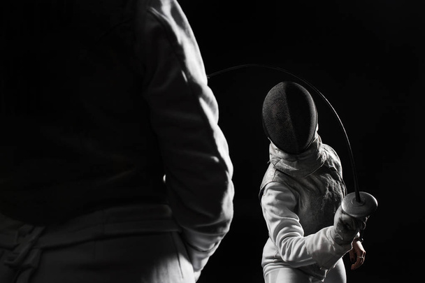 fencers wearing helmets and white uniforms fighting on black background - Фото, изображение