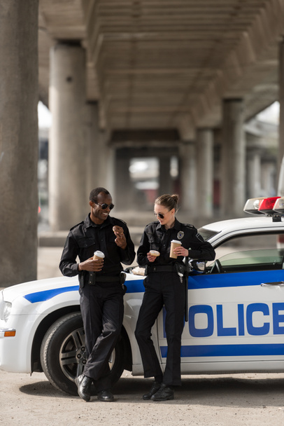 politieagenten met koffie en donuts permanent naast auto - Foto, afbeelding