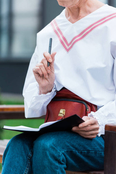 abgeschnittene Ansicht einer Frau im trendigen Outfit, die Tagebuch schreibt - Foto, Bild