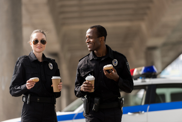 smiling police officers having coffee break with doughnuts - Foto, imagen