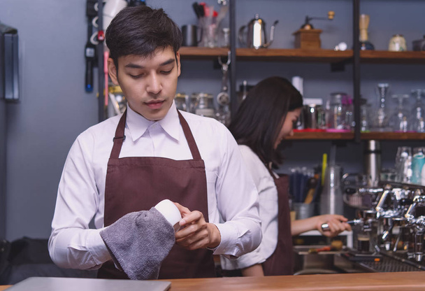 Portrait young barista cleaning cup coffee while standing - Photo, Image