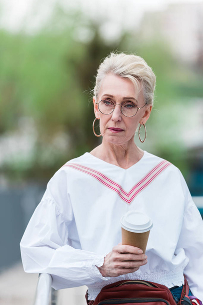 senior woman in trendy outfit with coffee to go walking in park - Photo, Image