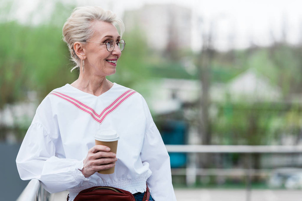 belle femme âgée en tenue tendance tenant tasse jetable de café dans le parc
 - Photo, image