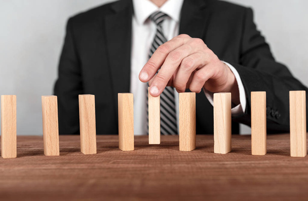 Businessman is placing wooden block in the center on a line of domino.Risk and business strategy concept. - Photo, image