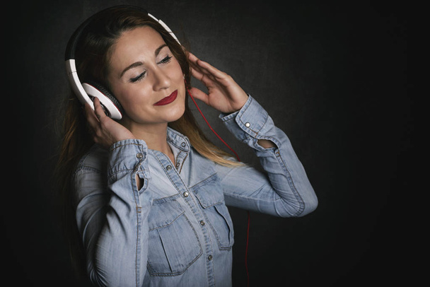 Happy young woman with headphones on black background - Photo, Image