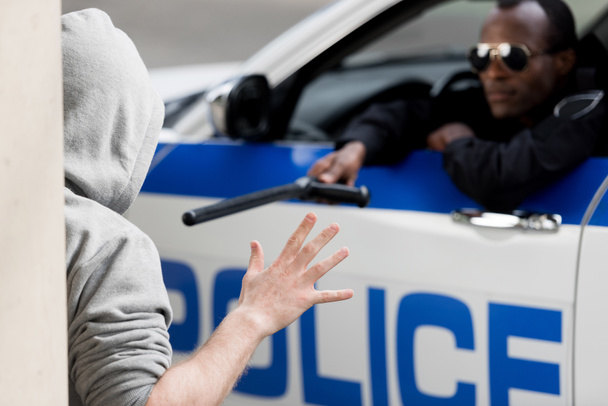 oficial de policía mirando por la ventana del coche y señalando al hombre encapuchado con bate de policía
 - Foto, imagen