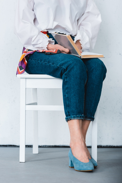 cropped view of woman sitting on chair with book - Fotó, kép