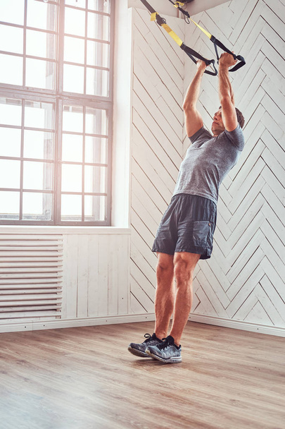 Aptitud muscular masculina haciendo ejercicio con TRX. Entrenamiento funcional en casa con bucles TRX
. - Foto, Imagen