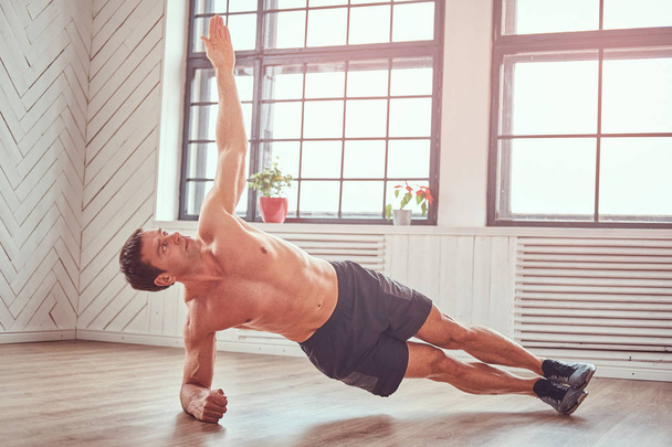 Handsome shirtless muscular man doing functional exercises on floor at home. - Foto, Imagen