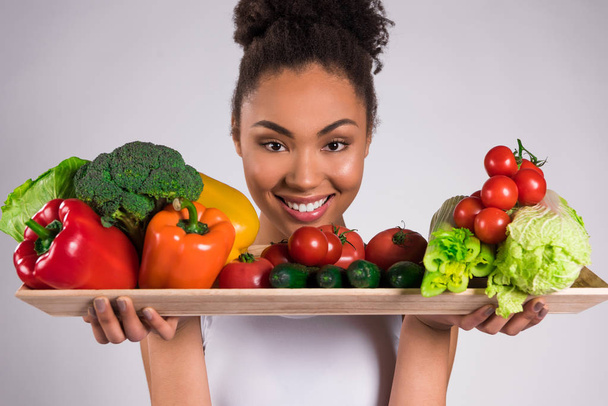 Black girl holding tray with vegetables isolated. - Foto, Imagen