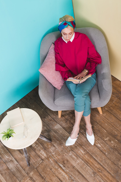 overhead view of senior woman reading book while sitting in armchair - Photo, Image
