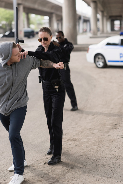 Женщина-полицейский с дубинкой арестовывает бандита и полицейского, стоящего позади и стреляющего из пистолета
  - Фото, изображение