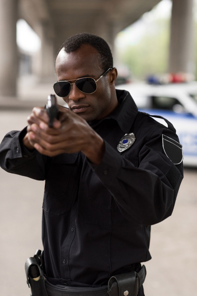 young african american policeman in sunglasses aiming by handgun  - Фото, изображение