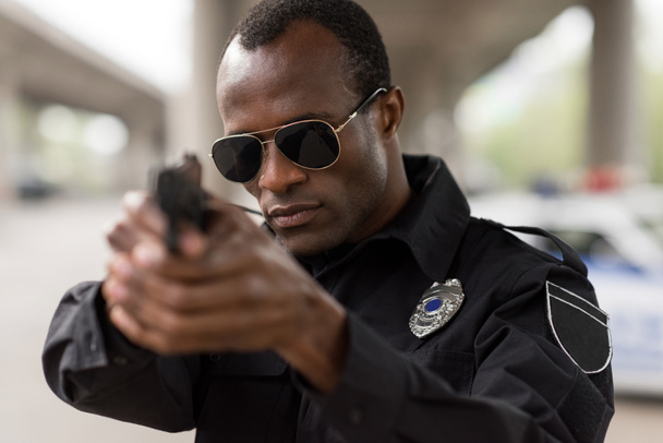 portrait of african american policeman in sunglasses aiming by handgun  - Foto, imagen