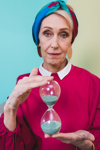 beautiful senior woman holding hourglass with blue sand - 写真・画像