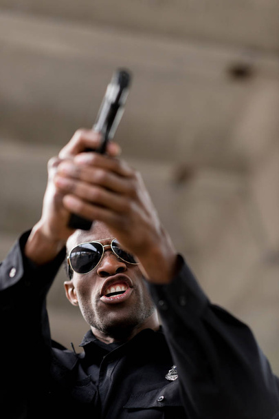 nízký úhel pohledu rozzlobený policista křičí a míření pistole  - Fotografie, Obrázek