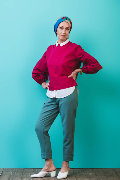 fashionable senior woman posing in room with turquoise wall - Фото, зображення