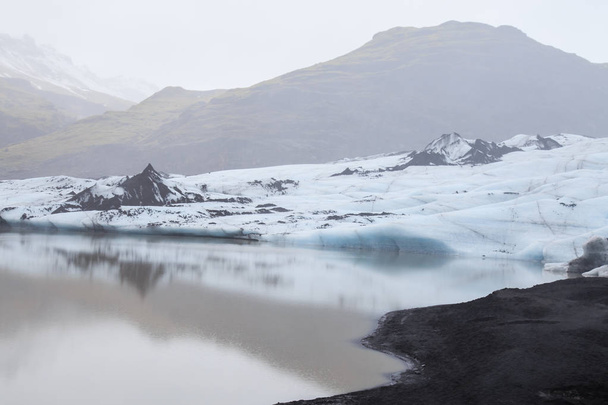 Hermoso paisaje silencioso del glaciar Slheimajkull con aguas tranquilas y aire brumoso, Islandia
. - Foto, Imagen