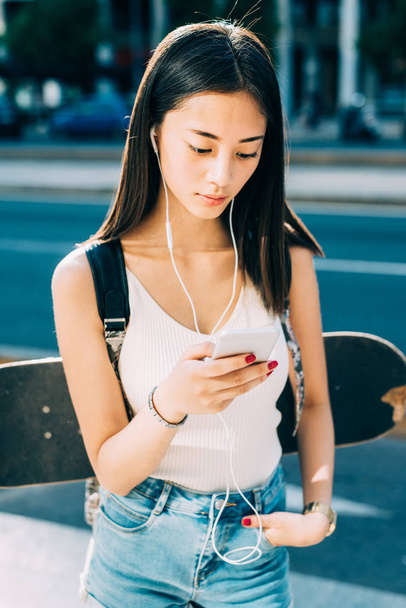 jonge vrouw lopen buiten gebruiken smartphone luisteren muziek - Foto, afbeelding