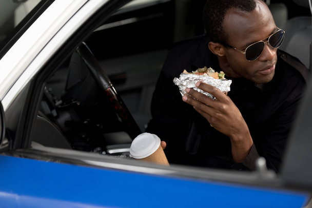 african american policeman in sunglasses having lunch in car  - Photo, Image